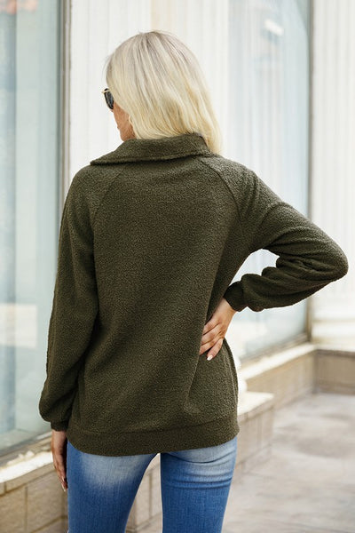 Rear view of a woman showcasing the back of an olive green asymmetrical neck sweater with jeans