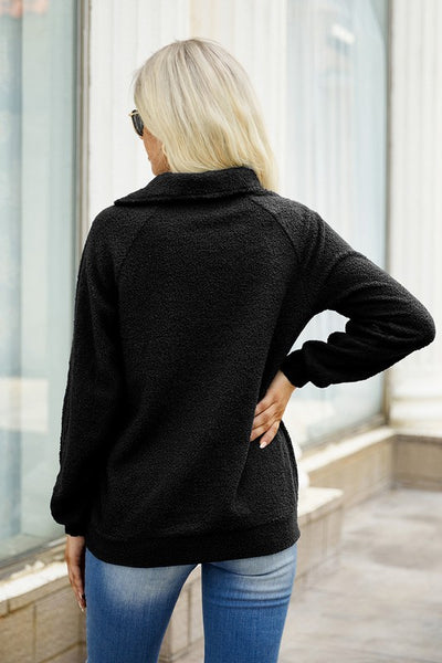 Woman standing with her back to the camera in a black asymmetrical zipper neck sweater